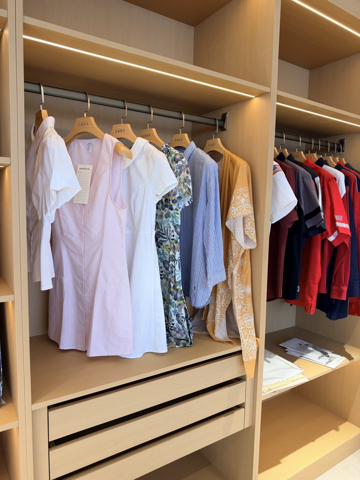 Pale pink shirt dresses, printed styles and casual tops displayed in wooden cabinets