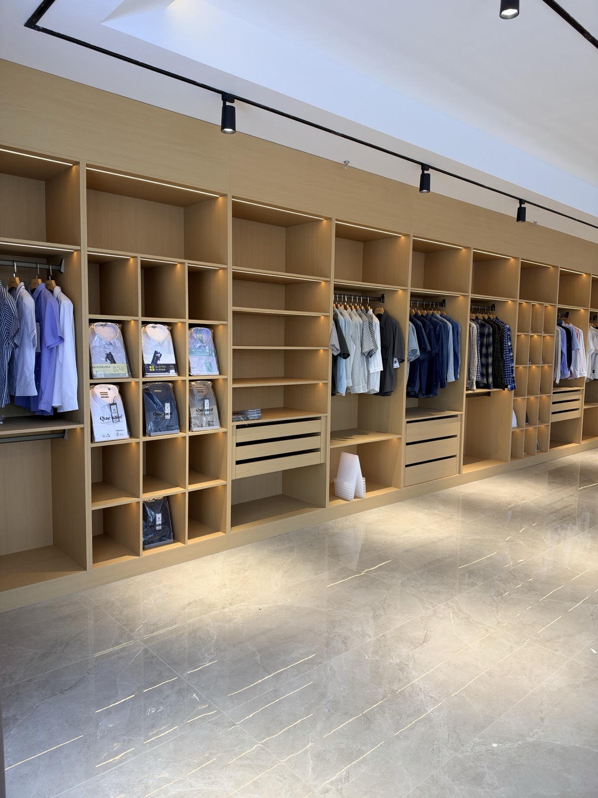 A wide view of the Mingsheng showroom with hanging shirts and folded samples in wooden cabinets